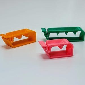 May include: Three plastic cable clips in orange, green, and pink. The clips are designed to hold cables in place.