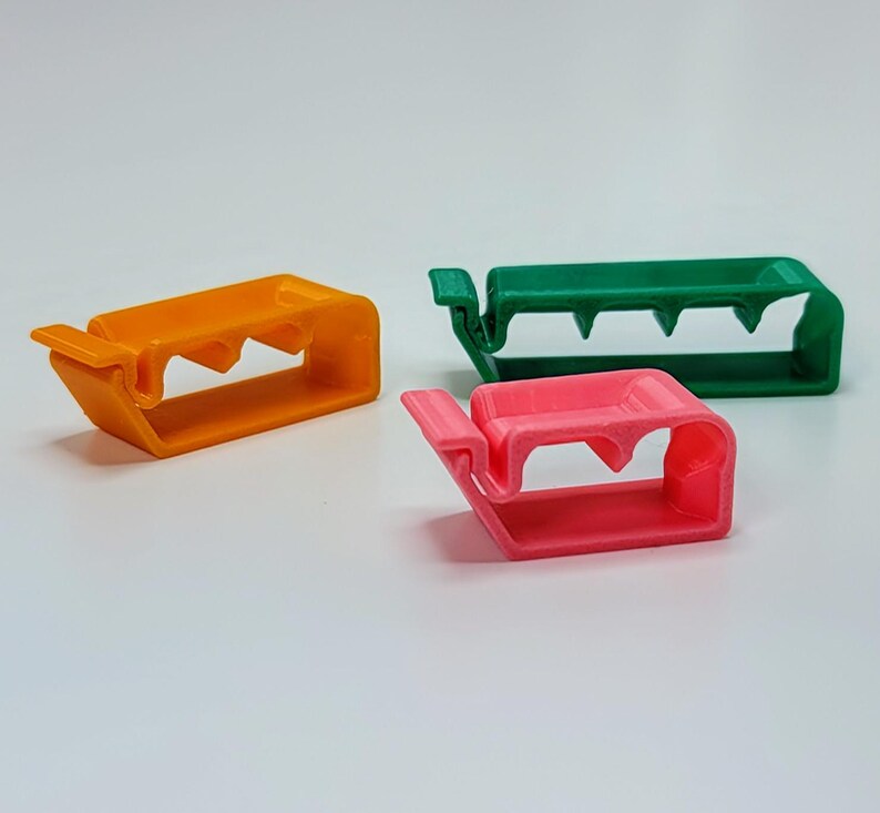 May include: Three plastic cable clips in orange, green, and pink. The clips are designed to hold cables in place.