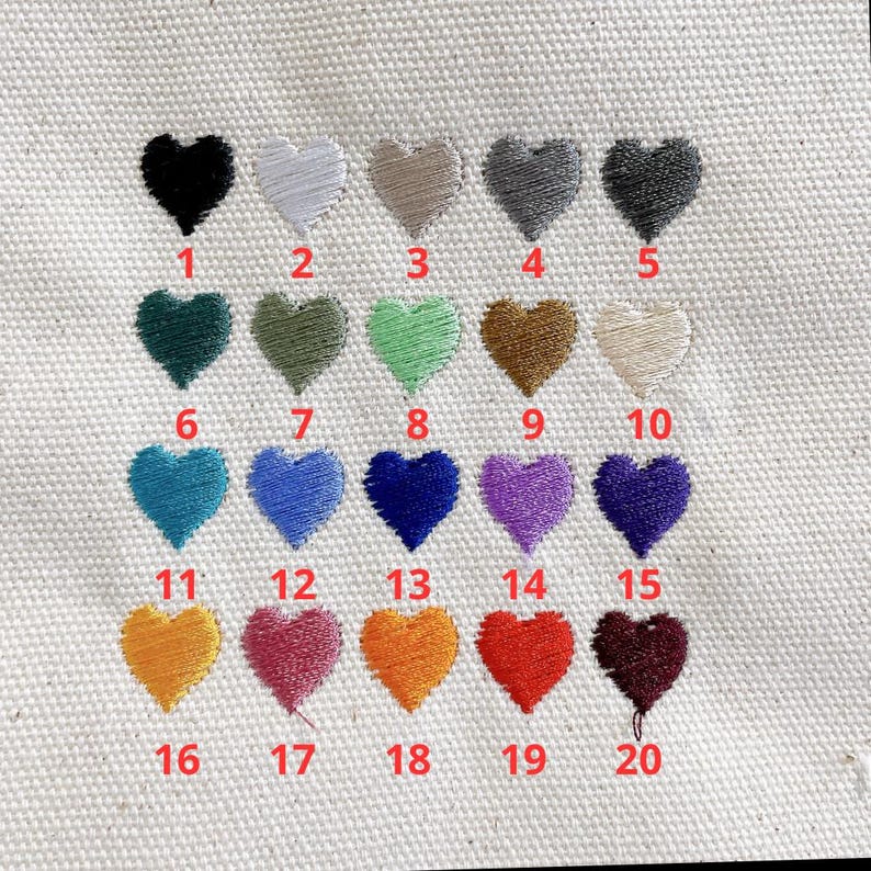 May include: Close-up of a canvas fabric with twenty embroidered heart shapes in various colors. Each heart is numbered from 1 to 20. Colors include black, white, gray, green, blue, purple, orange, red, and brown.