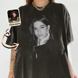 May include: Black t-shirt featuring a black and white portrait of a woman. The shirt has a distressed look and a small photo with the text "YOUR PHOTO" is in the upper left corner. The shirt is a relaxed fit.