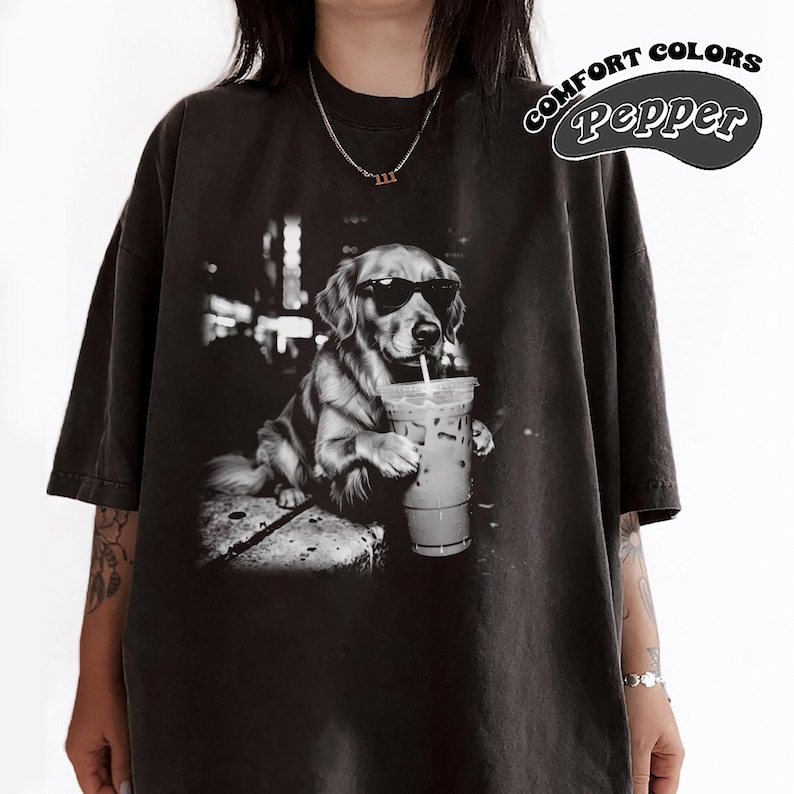 May include: Black t-shirt featuring a grayscale image of a Golden Retriever wearing sunglasses and drinking an iced coffee. The shirt has the words "COMFORT COLORS" and "Pepper" printed on the upper right side.