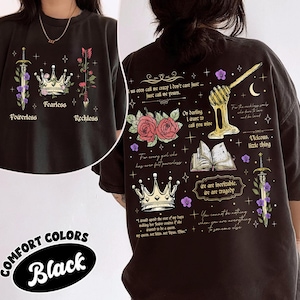 May include: Black graphic t-shirt with various illustrations and text. The front features a sword, crown, and arrow with the words "Powerless", "Fearless", and "Reckless". The back has additional graphics and quotes. The shirt is labeled "Comfort Colors Black".