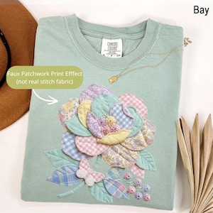 May include: A light green Comfort Colors t-shirt with a faux patchwork floral design. The design includes various pastel-colored fabrics, including gingham and floral prints. A gold necklace is draped on the shirt. The text "Faux Patchwork Print Effect (not real stitch fabric)" is visible.