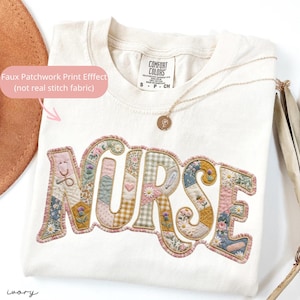 May include: Cream-coloured Comfort Colors t-shirt featuring the word "NURSE" in a faux patchwork design. The letters incorporate floral, gingham, and medical-themed patterns. A gold necklace with a pendant is also visible.