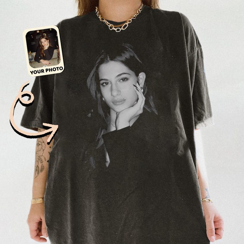 May include: Black t-shirt featuring a black and white portrait of a woman. The shirt has a distressed look and a small photo with the text "YOUR PHOTO" is in the upper left corner. The shirt is a relaxed fit.