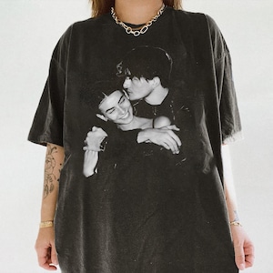 May include: Black oversized t-shirt featuring a black and white image of two people embracing. The graphic print is centered on the front of the shirt. The shirt has short sleeves and a crew neck.