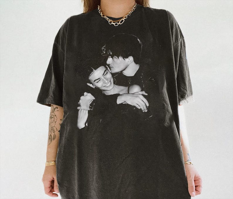 May include: Black oversized t-shirt featuring a black and white image of two people embracing. The graphic print is centered on the front of the shirt. The shirt has short sleeves and a crew neck.