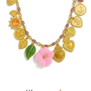 Peut inclure: Un collier en chaîne dorée avec de multiples breloques, dont des cœurs, des feuilles, un soleil, une lune et une fleur rose. Les breloques sont attachées à la chaîne avec de petites perles violettes. Le collier est de Charmania Jewels.