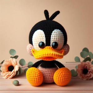 Puede incluir: Un juguete de peluche de ganchillo de un pato de dibujos animados con hilo negro, blanco, amarillo y rosa. El pato tiene ojos grandes y un pico amarillo.