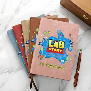 Könnte beinhalten: Eine Auswahl an personalisierten Notizbüchern in verschiedenen Farben, darunter Blau, Rot, Beige, Braun und Rosa. Das rosa Notizbuch zeigt den Text "Lab Story" mit einem wissenschaftlichen Design und dem Namen "Dr. Emily Johnson". Ein Holzstift liegt neben den Notizbüchern.