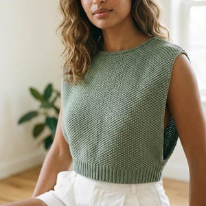 Peut inclure: Un gilet sans manches en tricot vert sauge avec un motif texturé en point de riz, une encolure ronde et un ourlet côtelé. Le vêtement est court et présente de larges emmanchures, mettant en valeur une construction en tricot uniforme sur l'ensemble.