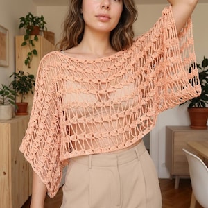 May include: A peach-coloured, open-weave crochet top with wide sleeves. The top has a round neckline and a loose, airy design, ideal for layering or warm weather. The crochet pattern creates a delicate, textured look.