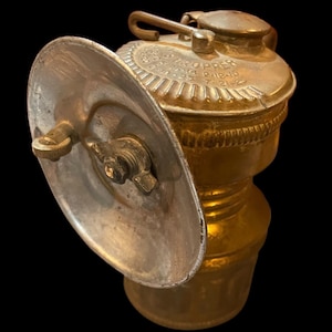 May include: Antique brass miner's headlamp with a round reflector and a  'C.G. STOPPERS P.1040 7-21-22' inscription.