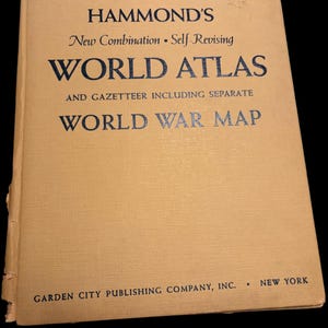 May include: A vintage world atlas with a tan cover. The title reads "HAMMOND'S WORLD ATLAS" in dark blue lettering. The cover also includes the text "WORLD WAR MAP" and "GARDEN CITY PUBLISHING COMPANY, INC. NEW YORK."