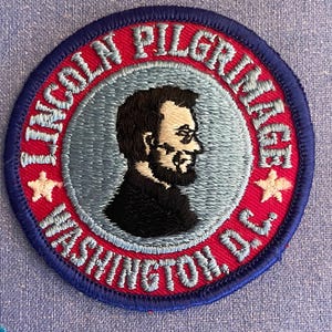May include: A red, white, and blue embroidered patch with the text "Lincoln Pilgrimage Washington, D.C." and a profile image of Abraham Lincoln.