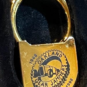 May include: Gold-colored keychain with a black and white image of a car and the text "1948 Oakland Gear Jammers 1998".