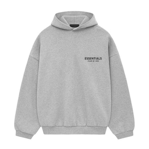 May include: A light gray hoodie with a hood and long sleeves. The text "ESSENTIALS FEAR OF GOD" is printed in black on the upper left chest area. The hoodie is made of a soft, comfortable material.