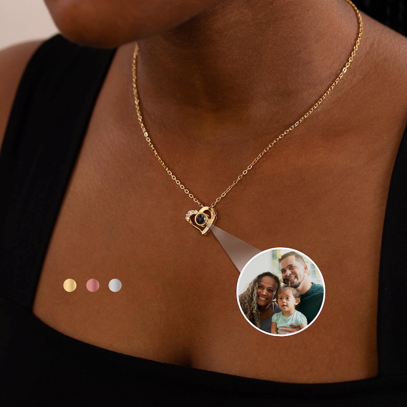Peut inclure: Un collier pendentif en forme de c&oelig;ur dor&eacute; avec une petite pierre noire et des cristaux transparents. Le collier est sur une cha&icirc;ne d&eacute;licate. Une petite image circulaire d'une famille est projet&eacute;e du pendentif.