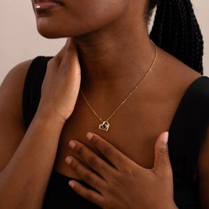 Peut inclure: Un collier dor&eacute; avec un pendentif en forme de c&oelig;ur. Le pendentif contient une pierre noire au centre et est entour&eacute; d'un cadre dor&eacute;. Le collier est port&eacute; autour du cou.