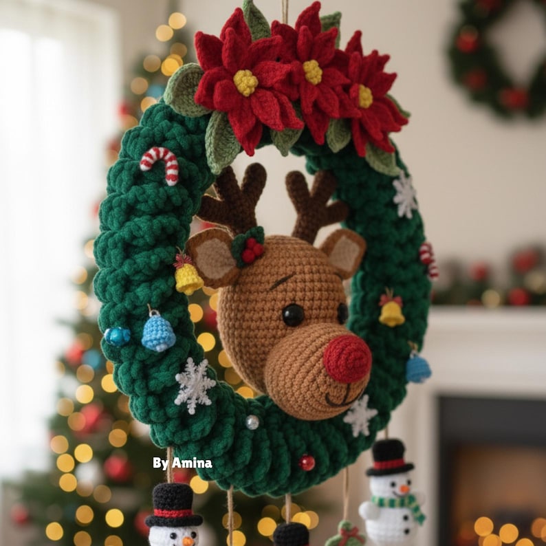 Op de afbeelding: Een handgemaakte kerstkrans met een gehaakte rendierkop, rode neus en geweien. De groene krans is versierd met rode poinsettia's, sneeuwvlokken en kleine ornamenten. De tekst "By Amina" is zichtbaar.