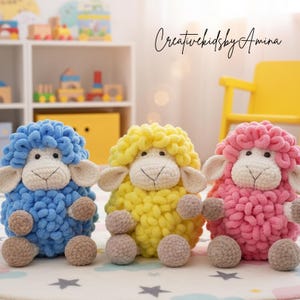 May include: Three handmade crochet sheep toys in blue, yellow, and pink. Each sheep has a fluffy, textured body, a white face, and small brown ball feet. The text "Creativekidsby Amina" is written in cursive.