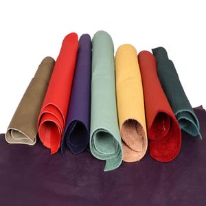 Può includere: Una collezione di pelli di cuoio arrotolate in vari colori, tra cui rosso, verde, giallo e viola. Le pelli sono disposte su un foglio più grande di cuoio viola. L'immagine è ben illuminata, mostrando le trame e i colori del cuoio.