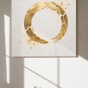 Könnte beinhalten: Ein quadratisches Wandbild auf Leinwand mit einem großen, strukturierten Kreis aus Blattgold auf schlichtem weißem Hintergrund. Der goldene Kreis wirkt aufgebrochen, mit verstreuten goldenen Farbspritzern, die von den Rändern der Form nach außen verlaufen.