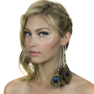 May include: A woman with blonde hair is wearing a pair of long, dangling earrings with peacock feathers. The earrings are silver chains with multiple peacock feathers attached to them. The feathers are green, blue, and brown.