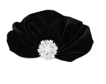 May include: A black velvet turban with a large, sparkly rhinestone brooch.