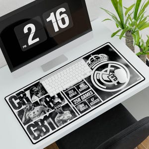May include: Black and white rectangular mousepad featuring the Real Madrid logo, player images, and statistics. The mousepad is on a white desk with a computer, keyboard, and mouse. The time on the computer screen reads 2:16 PM.