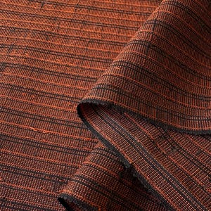 以下が含まれることがあります： 折りたたまれた織物のクローズアップ。生地は、錆と黒の色合いの細い水平線のパターンで、テクスチャ加工された外観をしています。生地の端が見え、織り方を示しています。