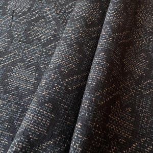 以下が含まれることがあります： テクスチャパターンが施された濃い青色の生地のクローズアップ。生地は織り込まれた外観で、小さな明るい色の斑点が微妙なデザインを作り出しています。生地の折り目は、画像に深さと奥行きを追加します。