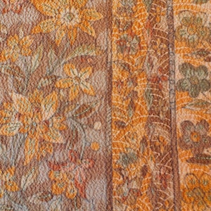 以下が含まれることがあります： 茶色、オレンジ、緑の色合いの、花柄のテキスタイルのクローズアップ。 デザインは、様式化された花と葉、さまざまなパターンの垂直ストライプを特徴としています。 生地は質感のある外観をしています。