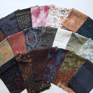 May include: A selection of folded fabric squares in diverse patterns and colours. The fabrics feature floral, geometric, and abstract designs in shades of blue, brown, red, and white. The squares are arranged in a fan shape.