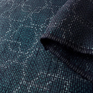 以下が含まれることがあります： 幾何学模様の濃い青とティール色のニット生地のクローズアップ。生地はリブ編みのテクスチャで、裏側を明らかにする折り畳まれた部分があります。パターンは白とティール色のステッチで作成されています。