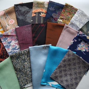 May include: A collection of rectangular fabric swatches arranged in a fan shape. The pieces feature diverse patterns including floral, geometric, and solid designs in colors such as navy blue, turquoise, brown, green, black, and light pink.
