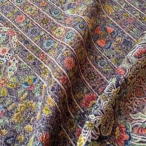 Peut inclure: Un tissu violet foncé présentant un motif floral dense et répétitif disposé en bandes verticales. Le design comprend de petites et grandes fleurs dans des tons orange, jaune, bleu clair et vert, créant un imprimé botanique texturé et multicolore.