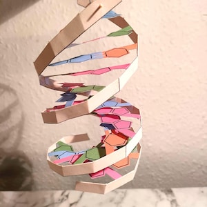 May include: A paper model of a DNA double helix, with a white base and coloured segments representing the different nucleotides. The model is suspended from the ceiling.