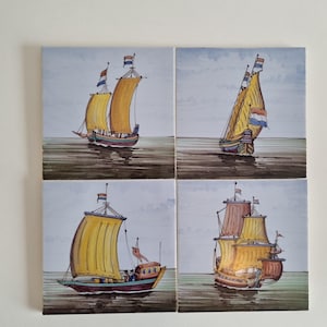 Op de afbeelding: Vier vierkante keramische tegels met illustraties van zeilschepen. Elk schip heeft gele zeilen, een bruine romp en een Nederlandse vlag. De schepen zijn afgebeeld op water onder een bewolkte hemel.