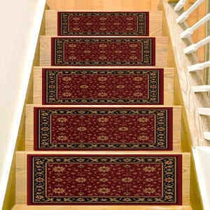 May include: Stair treads with a traditional design. The treads are rectangular, featuring a deep red field with a repeating floral pattern in gold and a black border. The treads are installed on wooden stairs.