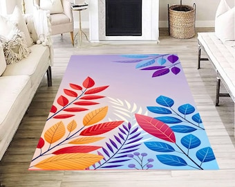 May include: A rectangular area rug with a gradient background of lavender to light blue. The rug features colorful leaf and branch designs in red, orange, yellow, purple, and blue. The rug is placed on a wooden floor.