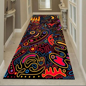 May include: A long, rectangular hallway rug with a black background and a vibrant, abstract design. The pattern features colourful, swirling shapes in red, yellow, blue, and orange. The rug is placed in a hallway with white walls and doors.