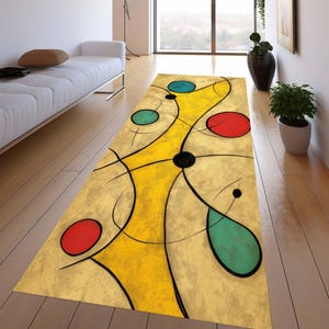 May include: A rectangular abstract art rug with a beige background. The rug features a yellow central design with black lines and colorful circles in red, teal, and blue. The rug is placed on a wooden floor.