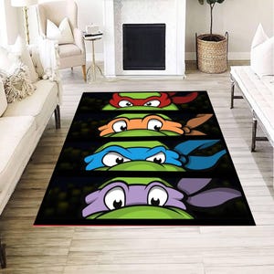 Puede incluir: Una alfombra rectangular con cuatro paneles horizontales, cada uno mostrando los ojos y las máscaras de colores de las Tortugas Ninja. Las máscaras son rojas, naranjas, azules y moradas, sobre un fondo oscuro con piel de color verde.