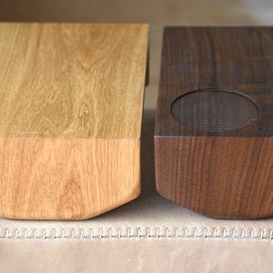 May include: Two wooden boxes, one light-colored and one dark, sit side-by-side. The light box has a natural wood grain, while the dark box has a carved indentation on top. Both have a curved bottom edge. The boxes are likely for storage or display.