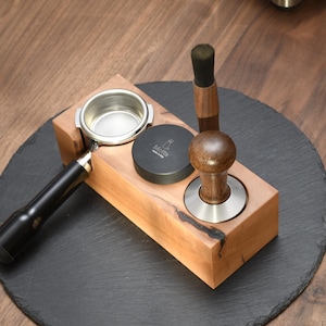 Op de afbeelding: Een houten espressostation met een portafilter, een tamper en een zwart puckscherm. Het station is gemaakt van lichtgekleurd hout en staat op een donkergrijze leistenen onderzetter. De tamper heeft een houten handvat en een roestvrijstalen basis.