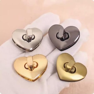 May include: Four heart-shaped metal clasps in silver, gunmetal, and gold tones. Each clasp has a rectangular bar and a circular loop for closure. The clasps are displayed on a white surface.