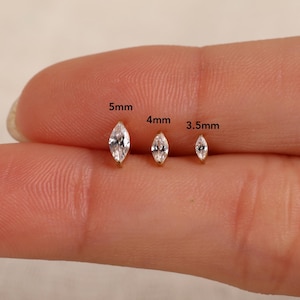 May include: Three marquise-cut clear gemstones set in gold metal, labeled with sizes 5mm, 4mm, and 3.5mm. The stones are arranged in a row, showcasing their elongated, pointed shape and faceted surfaces that reflect light, providing a clear visual size comparison.