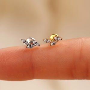 May include: Two stud earrings featuring a leaf-like arrangement of three marquise-cut clear stones. One earring is silver-toned metal, and the other is gold-toned metal. Each stud has a flat circular backing visible behind the stone cluster.