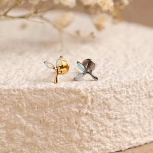 May include: Two stud earrings featuring a branch-like design with three small, iridescent, oval-shaped stones. One earring is gold-toned, and the other is silver-toned. Each piece has a flat circular backing and a curved stem structure.